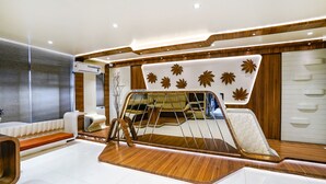 Quarto moderno com piso de madeira, sofá, cama com cabeceira estampada com padrão de folhas e uma janela com persianas.