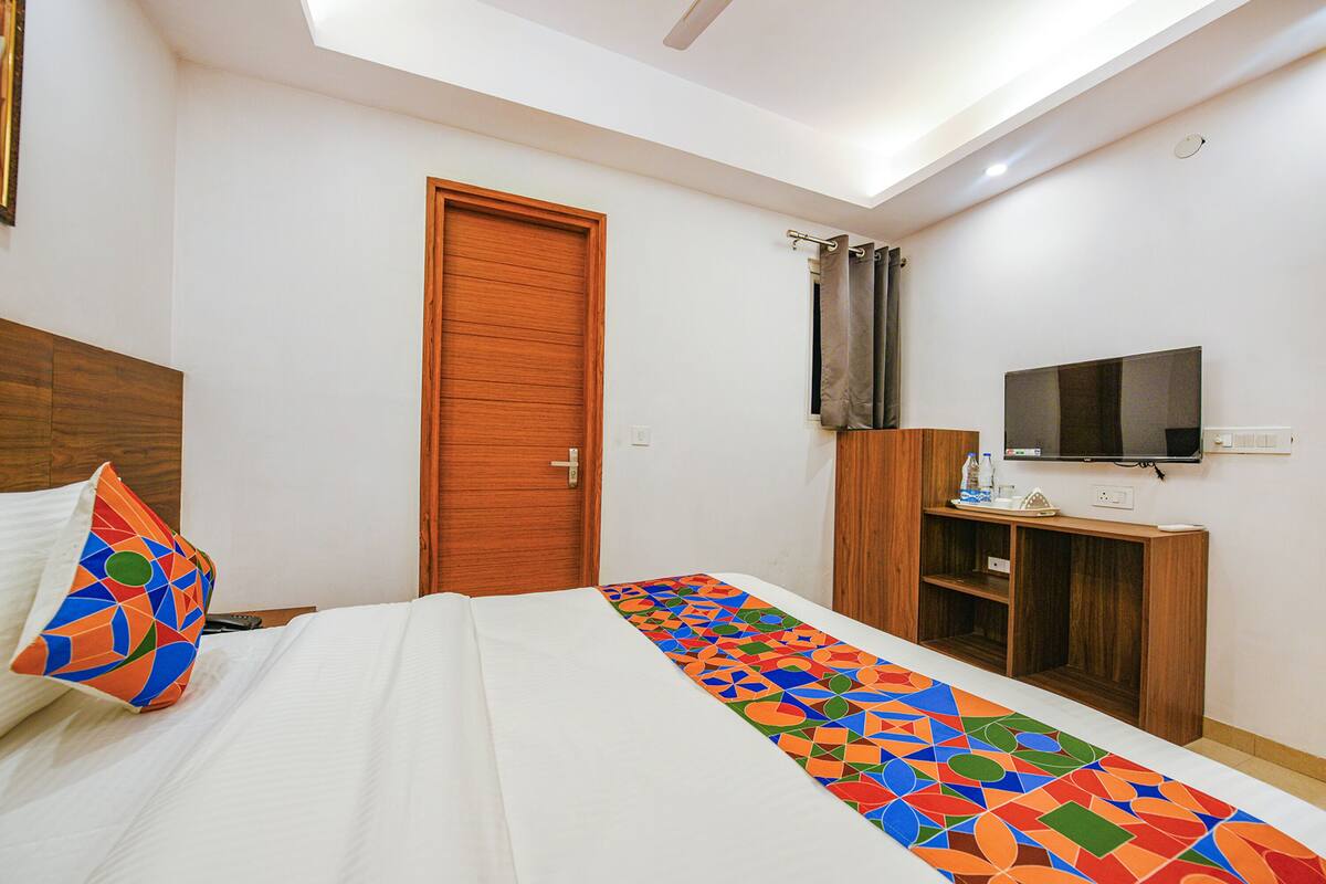 A hotel room with a bed, a TV, a wooden wardrobe, and a door.