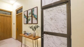 A hallway with a wooden door, a marble-framed glass door, and a small table with books and a vase. - FabHotel Rameshwaram Guest House - 500m From Ram Mandir (Faizabad)