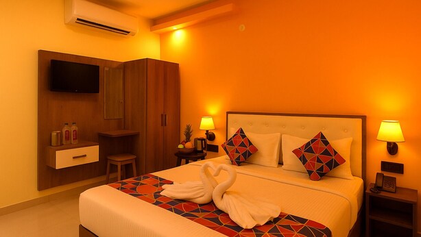 A hotel room with a bed, a TV, a wardrobe, a nightstand, and a lamp. - FabHotel Rameshwaram Guest House - 500m From Ram Mandir (Faizabad)