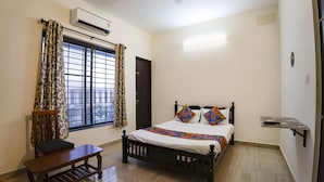 Un dormitorio con cama, una silla, una ventana con cortinas, un aire acondicionado y un ventilador de techo.
