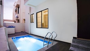 Una pequeña piscina interior con suelo azul, una escalera metálica y una puerta de madera oscura.