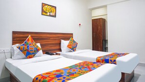 A hotel room with two beds, a wooden headboard, a painting of flowers on the wall, and a wardrobe. - Fabhotel Everest Inn (Pune)