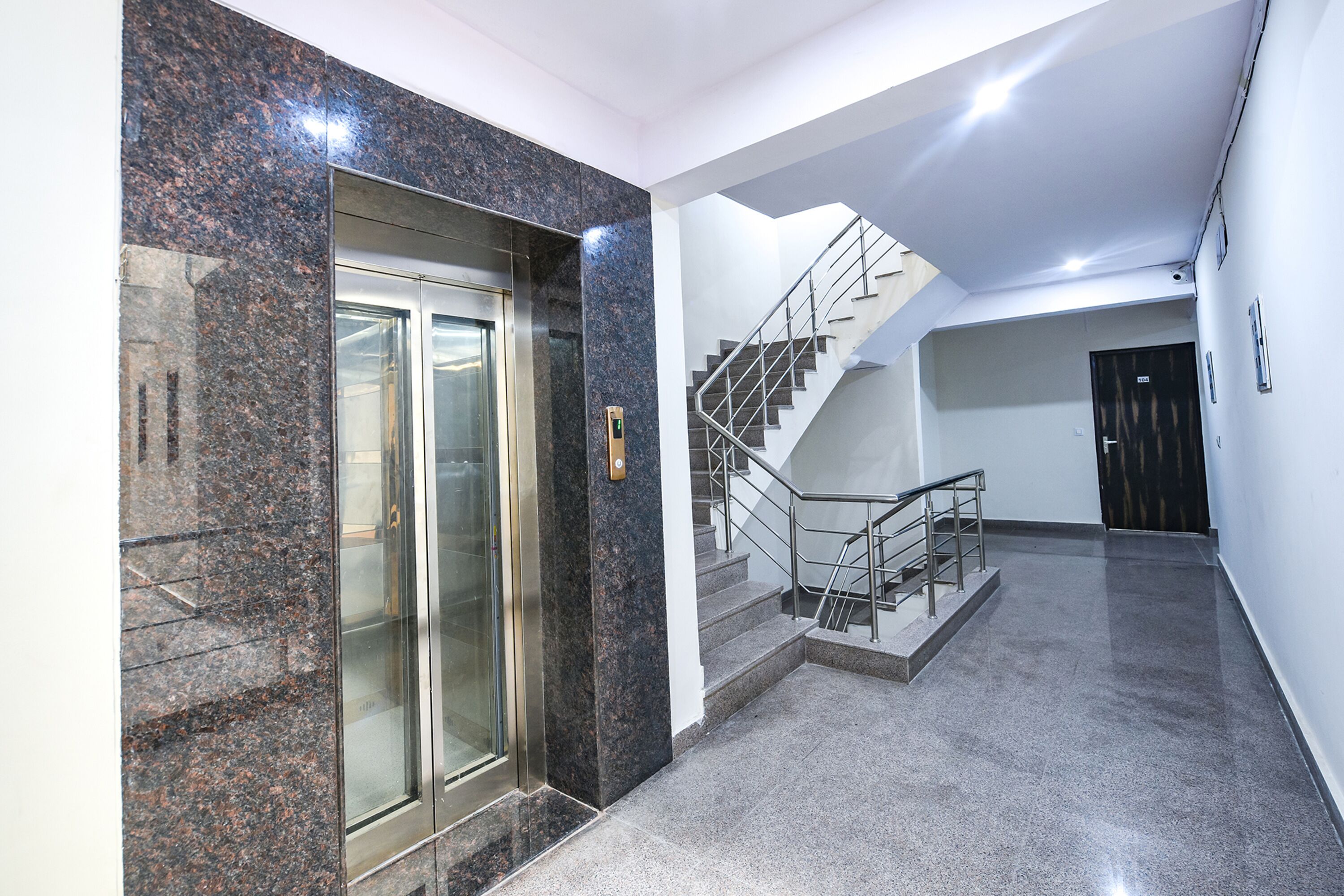 Un interior moderno con un ascensor de mármol, una escalera y una pared lisa.