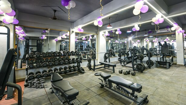 Een sportschool met diverse fitnessapparaten, spiegels en een plafond versierd met ballonnen.
