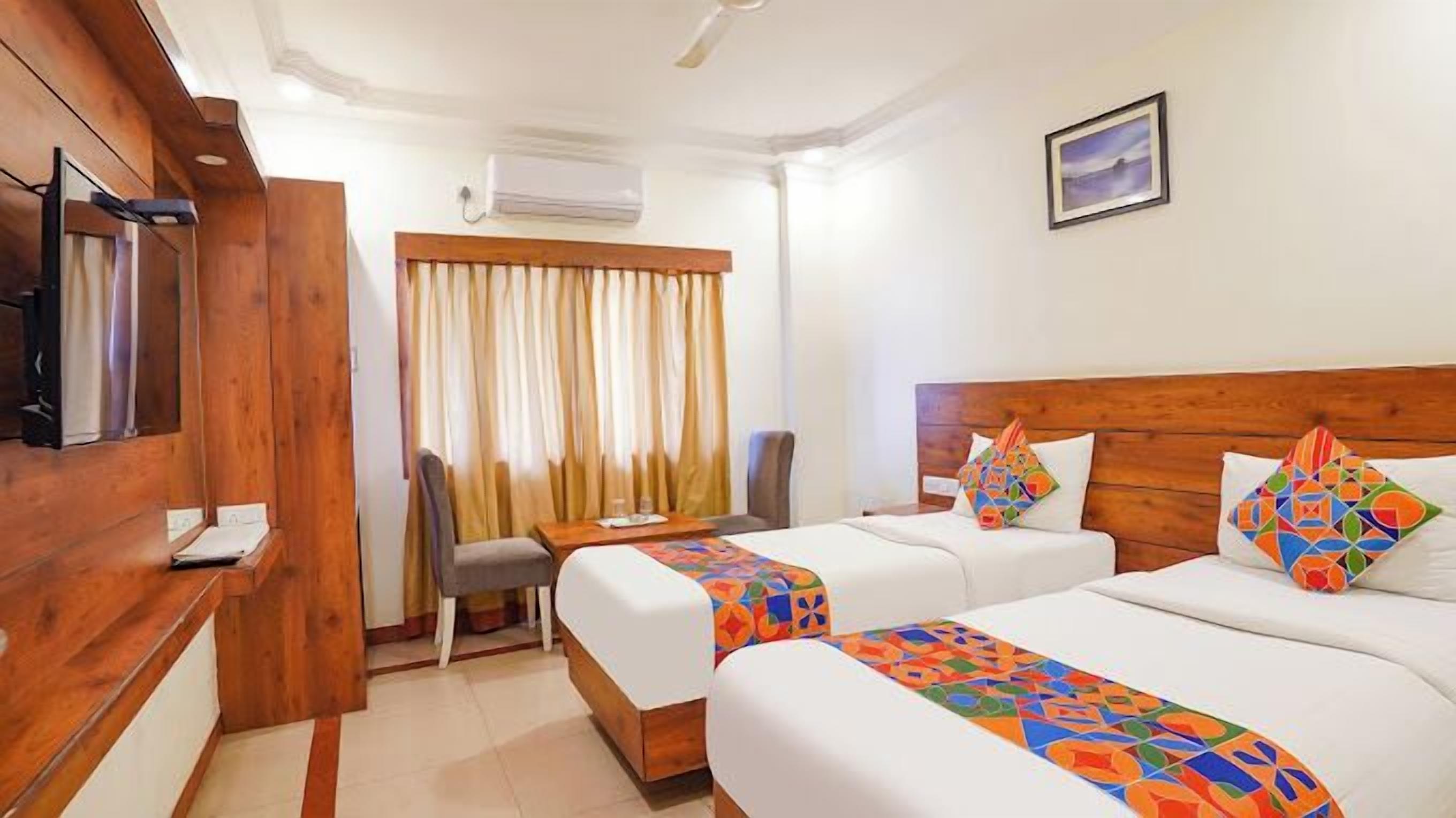 A hotel room with two beds, a desk, a chair, a TV, and a window with curtains.