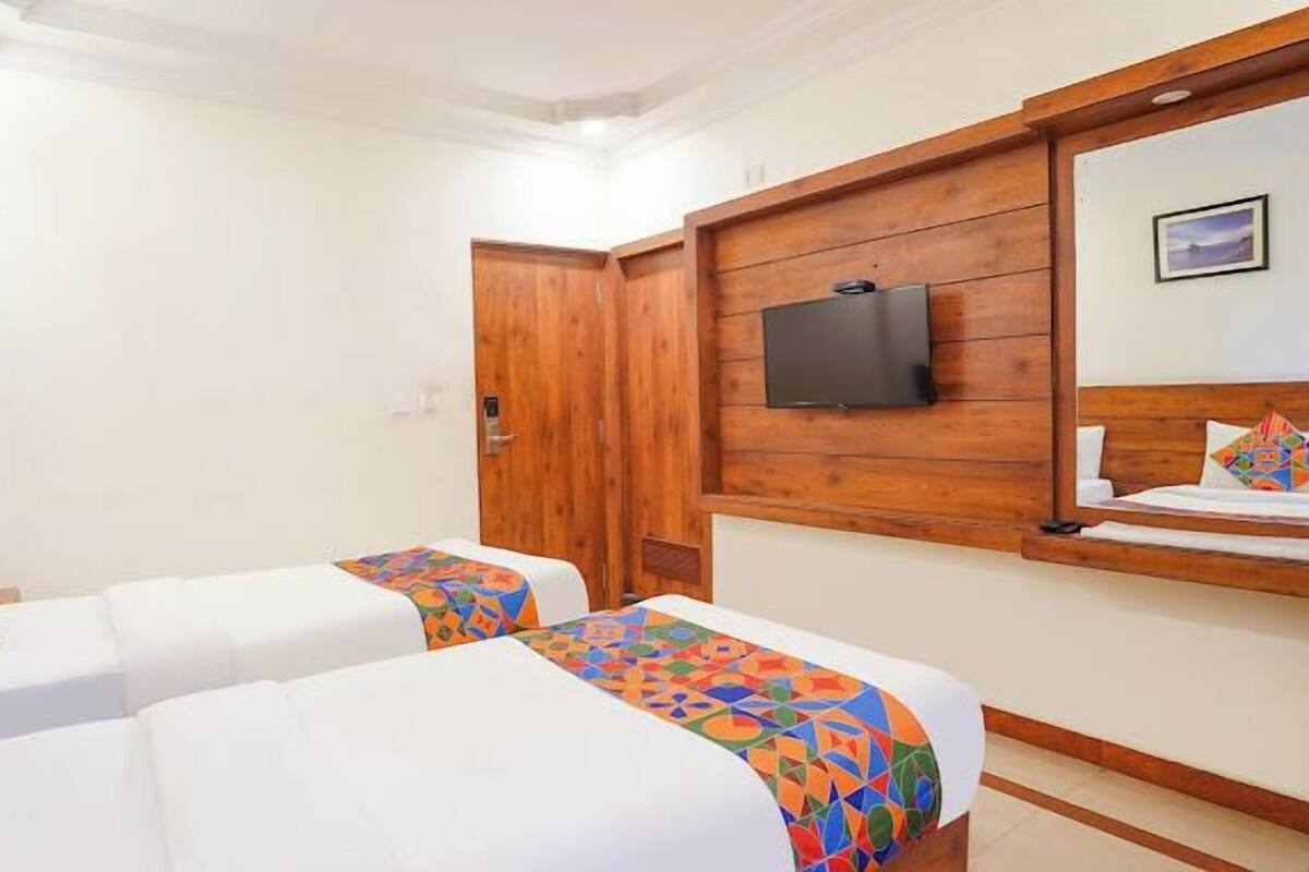 A hotel room with two beds, a television mounted on the wall, and a wooden door.