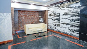 Un hall con suelo de mármol negro, un sofá blanco, un ventilador y una pared de ladrillo.