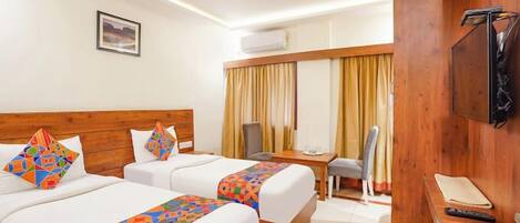 A hotel room with two beds, a desk, a chair, a TV, and a ceiling fan.
