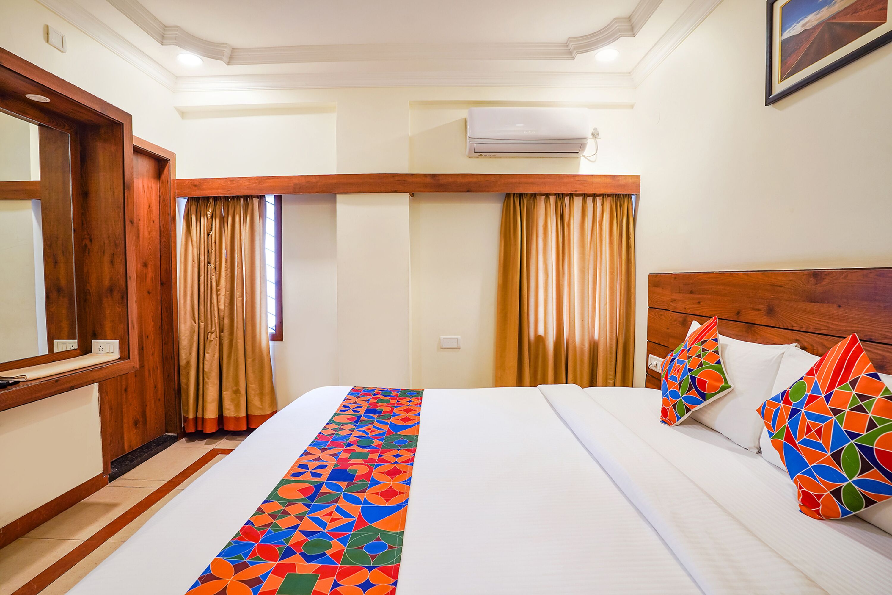 A hotel room with a large bed, wooden headboard, and a colorful bed runner.