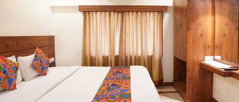 A hotel room with a bed, a wooden wardrobe, a desk, and an air conditioning unit.