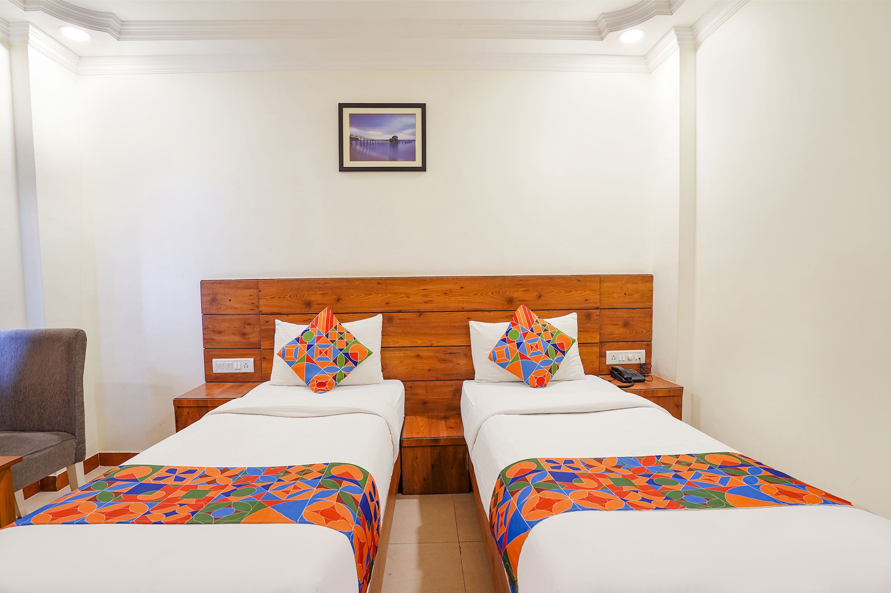 A hotel room with two beds, a wooden headboard, a framed picture on the wall, and a chair.