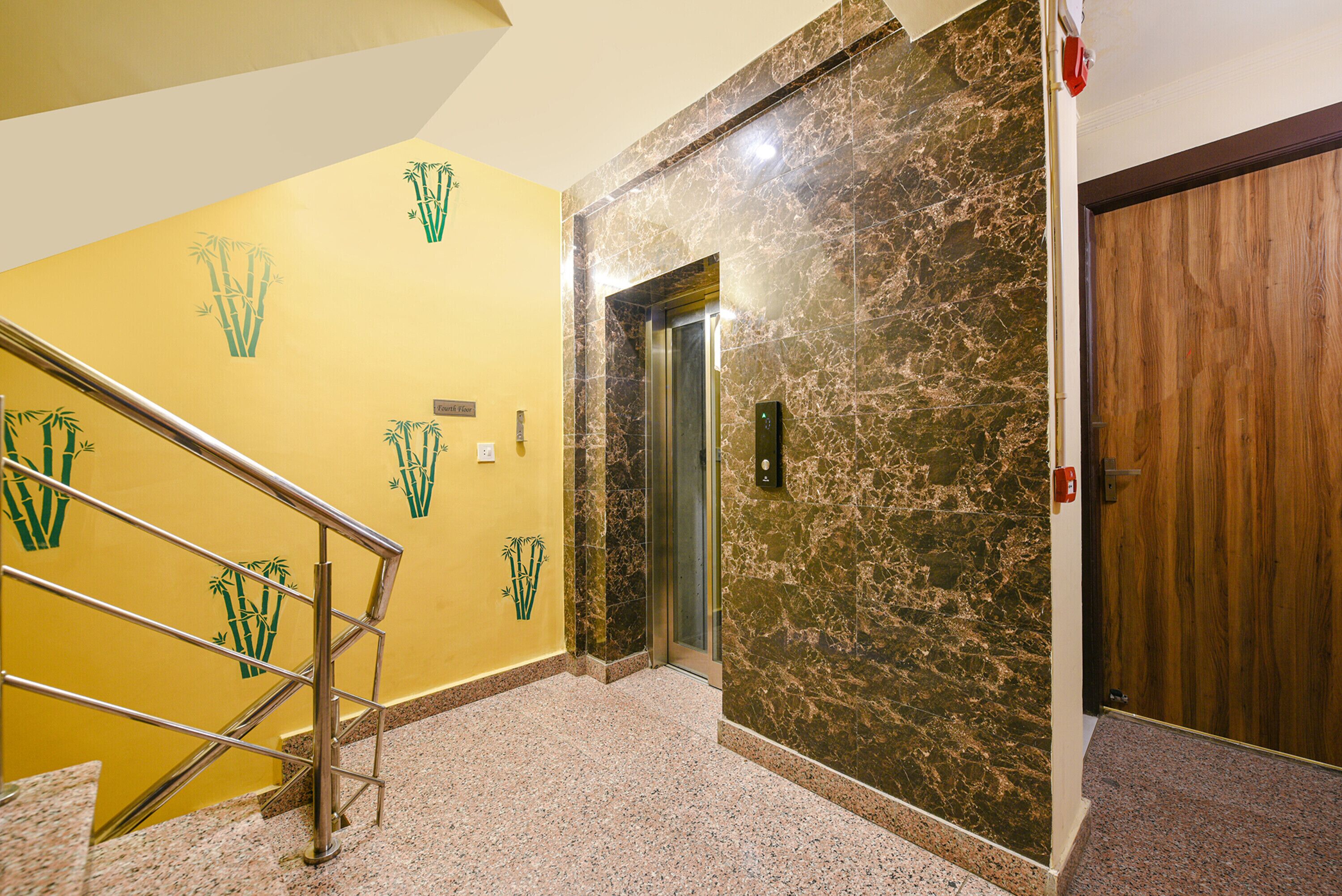 A hotel lobby with a marble wall, a wooden door, and a staircase with a metal railing.
