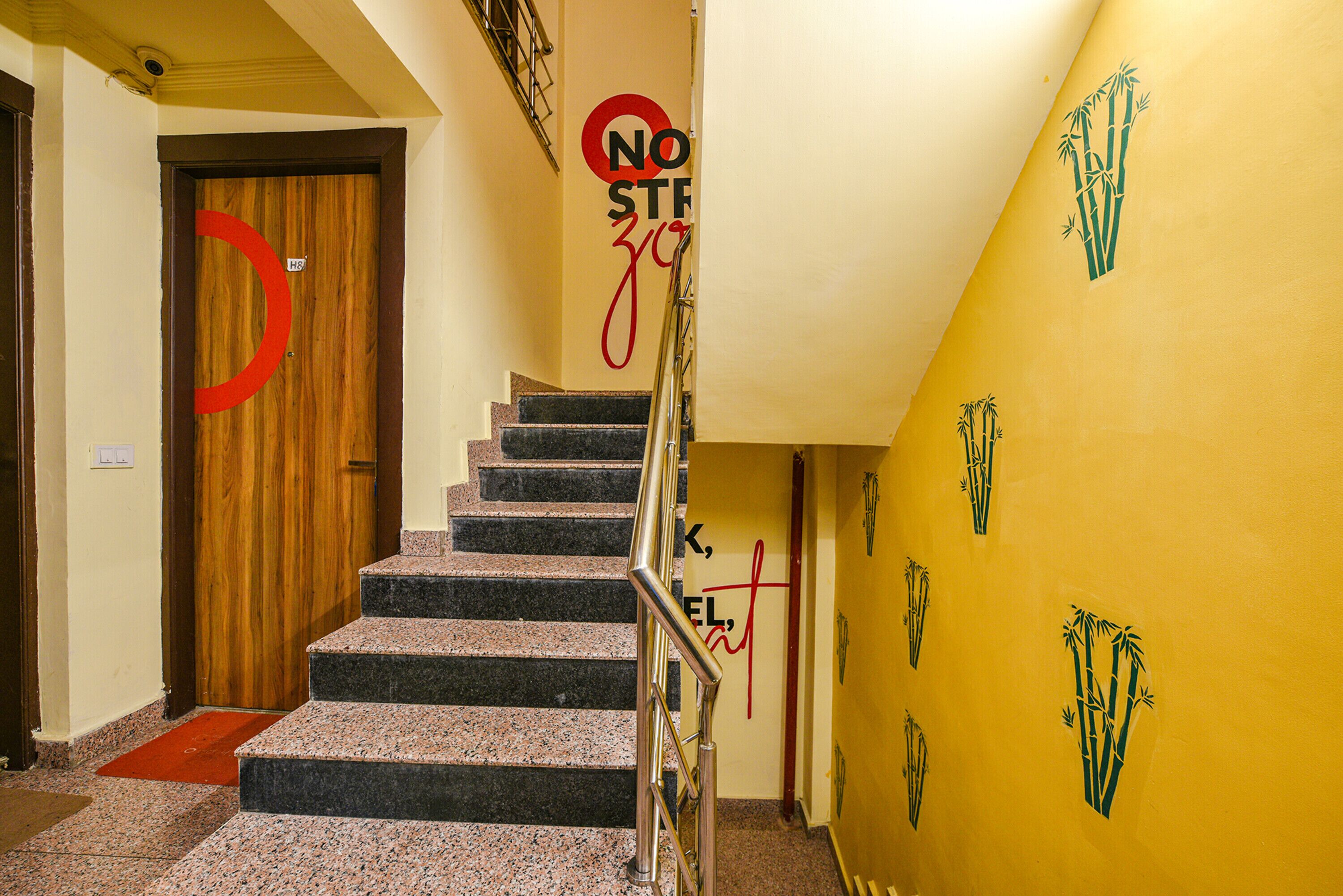A staircase with a wooden door at the top, a red circular sign, and a yellow wall with bamboo graphics.