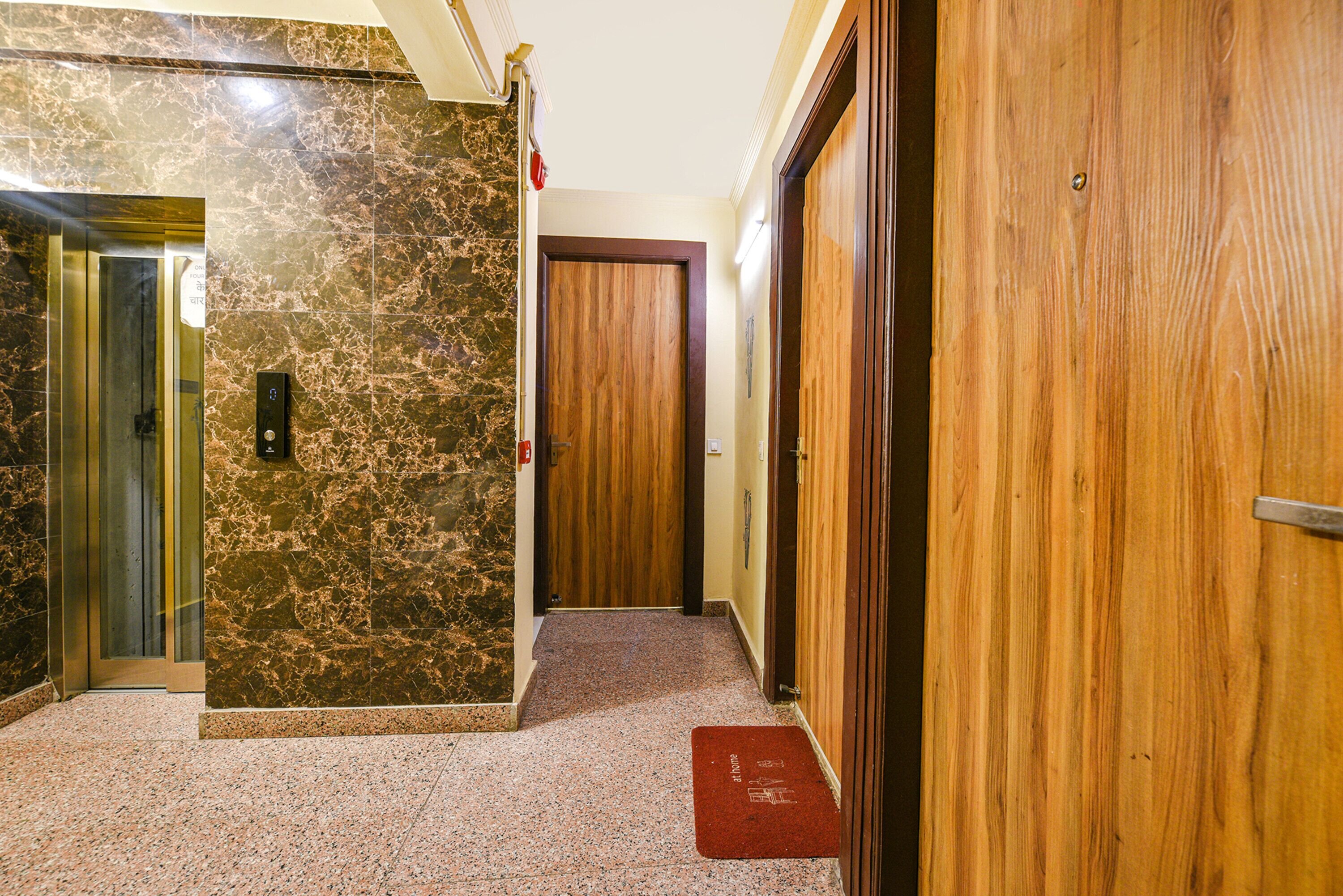 A hallway with a marble wall, a wooden door, and a red mat at the entrance.