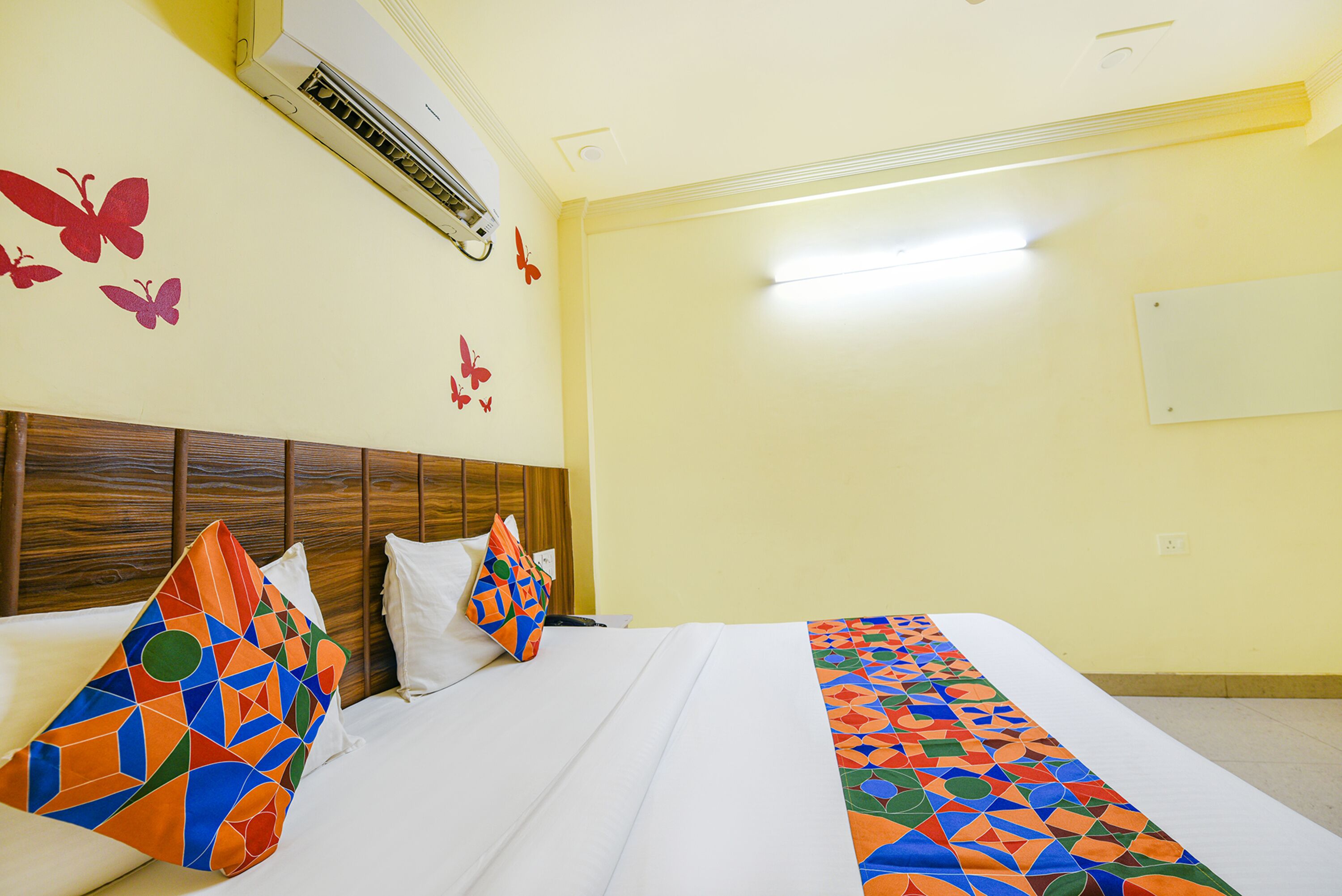 A hotel room with a wooden headboard, a bed with white linens, colorful geometric pillows, and butterfly wall decals.