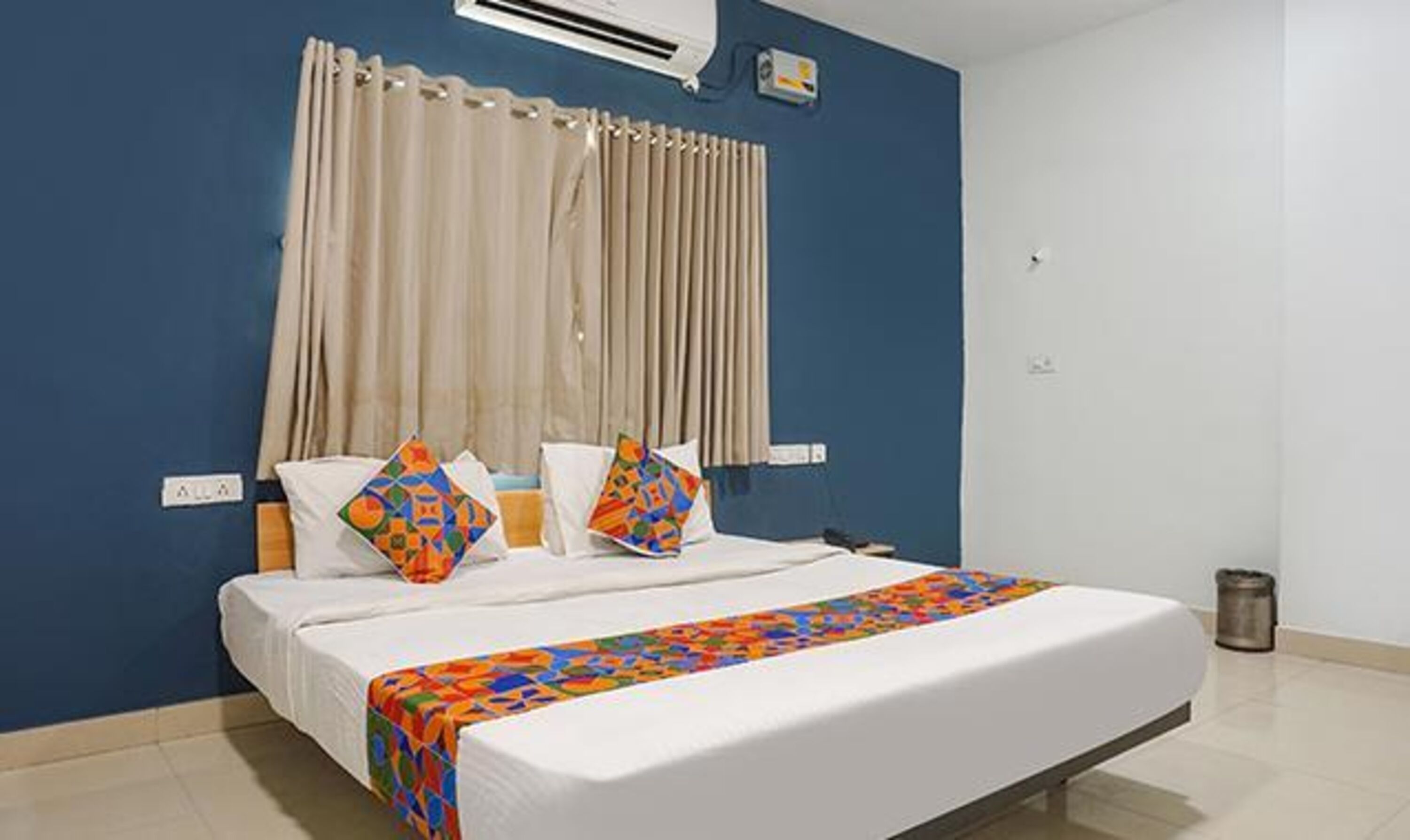 A hotel room with a bed, curtains, and an air conditioning unit.