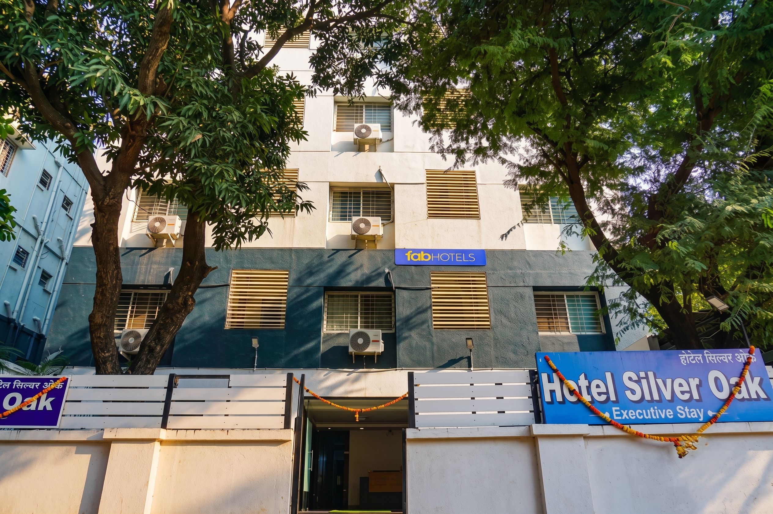 A building with multiple air conditioning units, a sign for FabHotels, and a sign for Hotel Silver Oak.