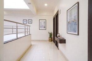 A corridor with a staircase, framed pictures on the walls, a potted plant, and a small shelf with books. - Fabhotel Silver Oak (Pune)