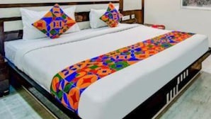 A hotel room with a bed, wooden slats on the wall, a window with a patterned curtain, and a wall-mounted air conditioning unit. - FabHotel Trishiv - Newtown Kolkata (Barasat)