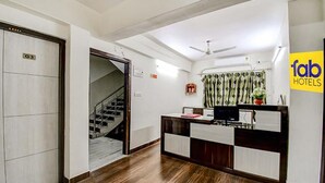 A hotel reception area with a reception desk, a staircase, and a ceiling fan. - FabHotel Trishiv - Newtown Kolkata (Barasat)