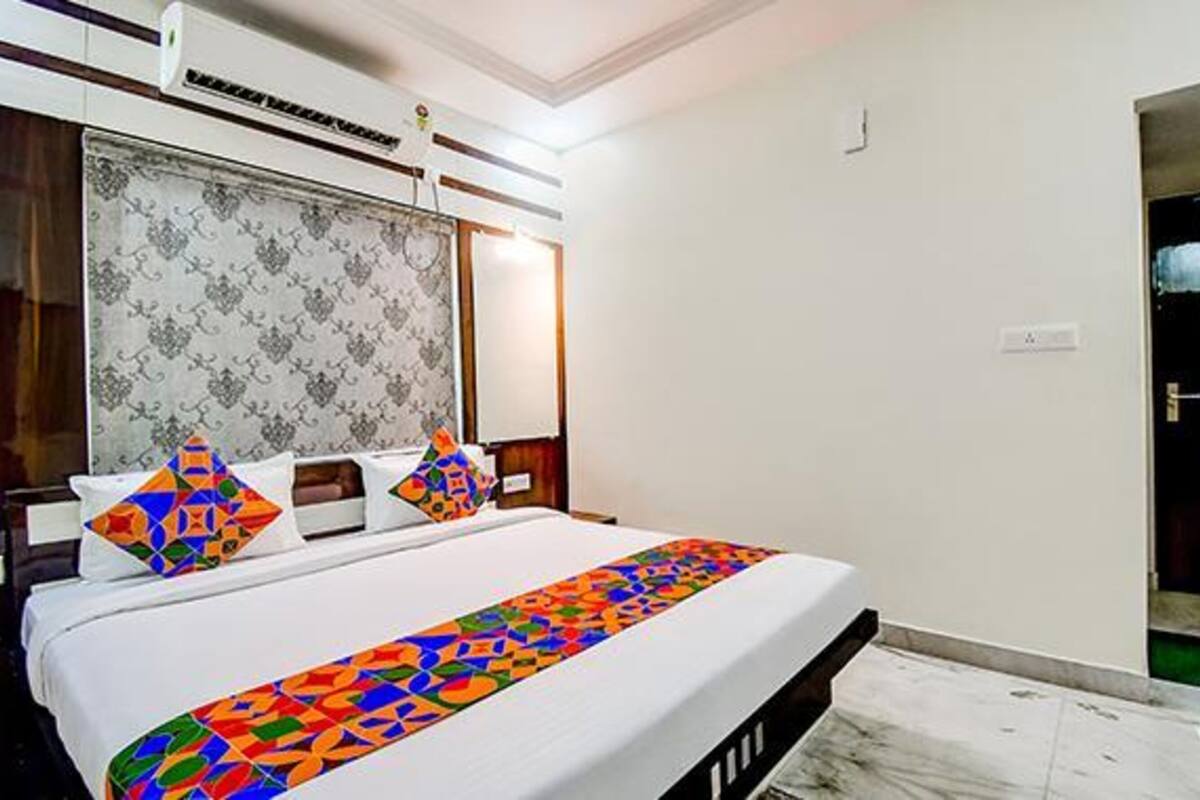 A hotel room with a bed, a patterned headboard, a decorative pillow, and a colorful bed runner.