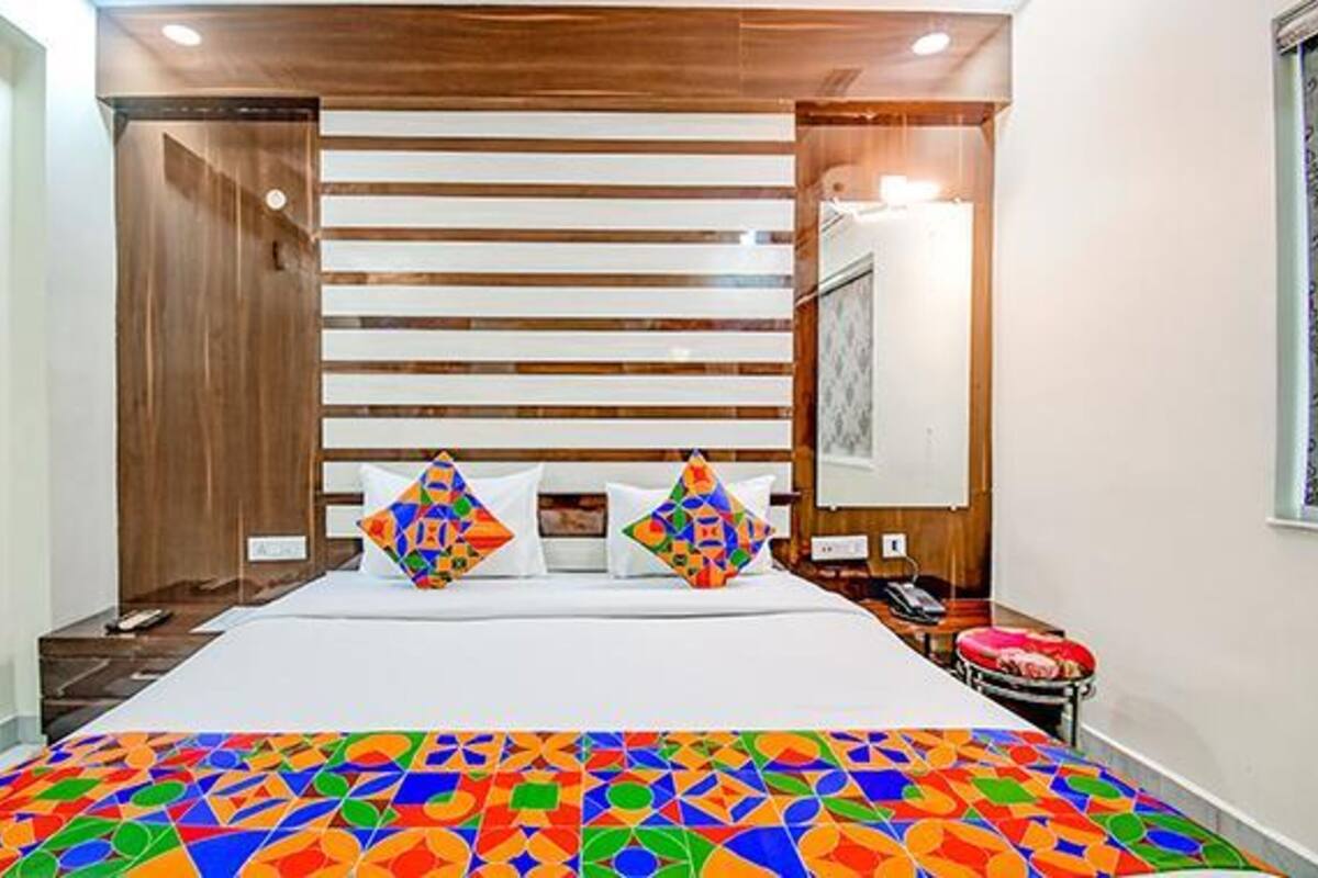 A hotel room with a bed, a bedside table, a nightstand, and a small stool.