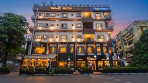 Un hotel de varios pisos con restaurante en la azotea, un restaurante visible llamado "The Bacon", y un letrero que dice "FatihHotels".