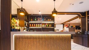 Una zona de bar con un mostrador de recepción de madera, estanterías con botellas e iluminación colgante.