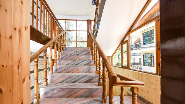 A wooden staircase with a view of the outdoors through large windows. - Fabhotel Hadimba Heights (Manali)