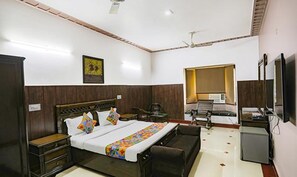 Habitación de hotel con cama, escritorio, silla, televisión y ventilador de techo.