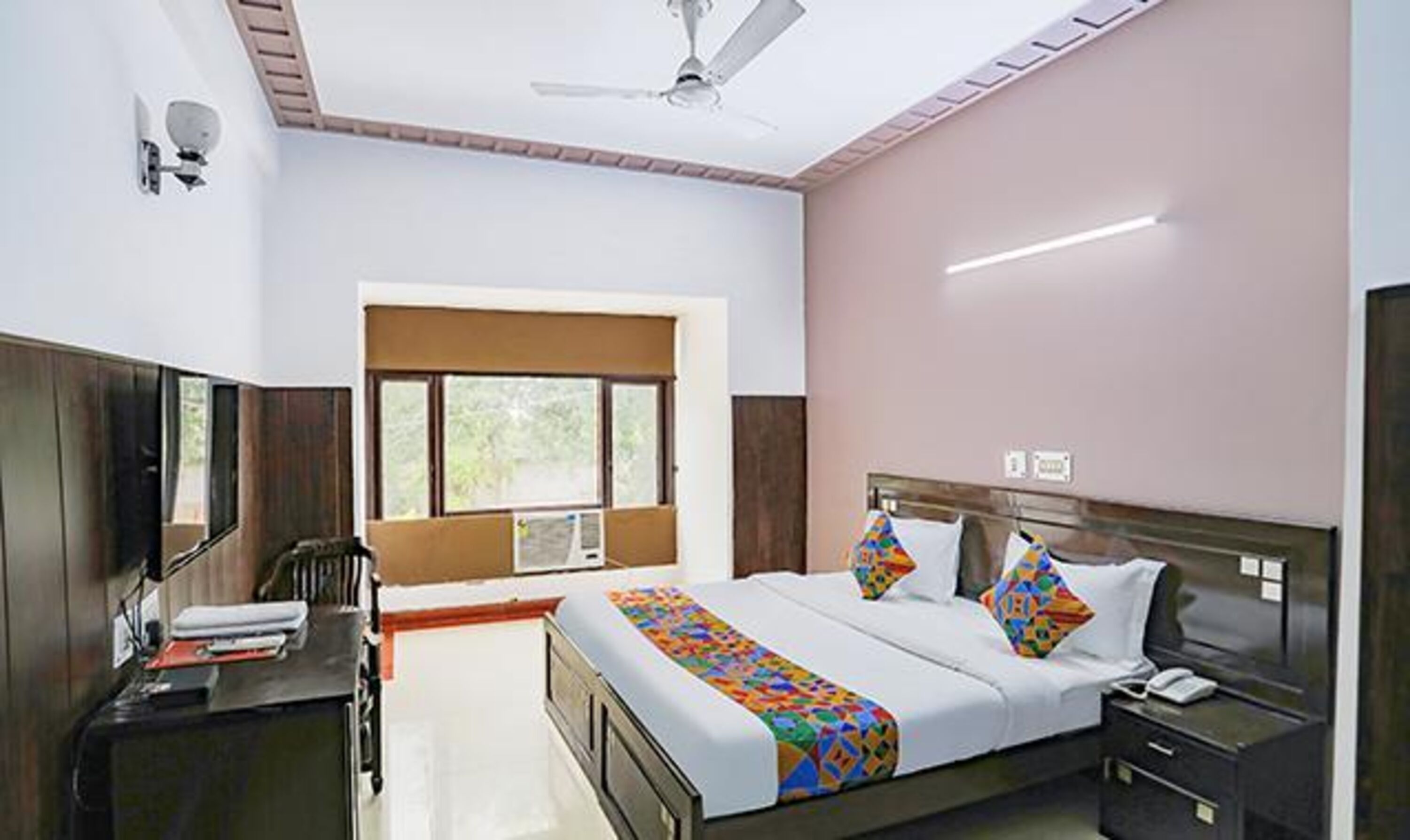 A hotel room with a bed, bedside table, desk, chair, window, and ceiling fan.