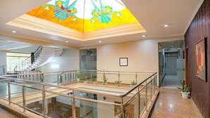 Spaziosa hall con ringhiera in vetro, una scala e un soffitto decorato con motivi floreali.