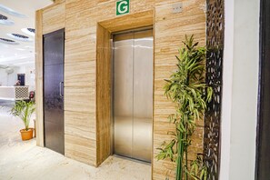 An elevator with a green 'G' sign, a potted plant, and a decorative bamboo wall. - Fabhotel Idea Inn (Agra)