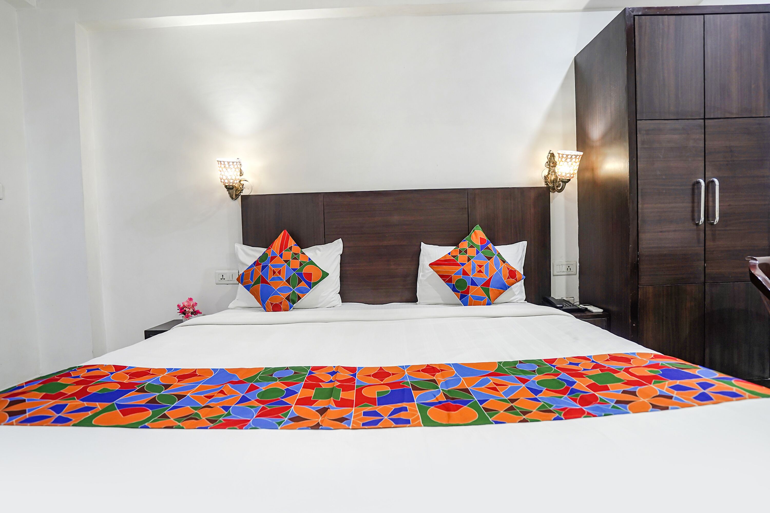 Une chambre d’hôtel avec un grand lit, deux coussins décoratifs, une table de chevet, une armoire et des appliques murales.