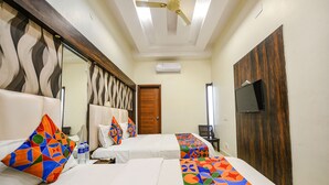 A hotel room with two beds, a ceiling fan, an air conditioning unit, a TV mounted on the wall, and a wooden door. - Fabhotel Savera Park (Amritsar)
