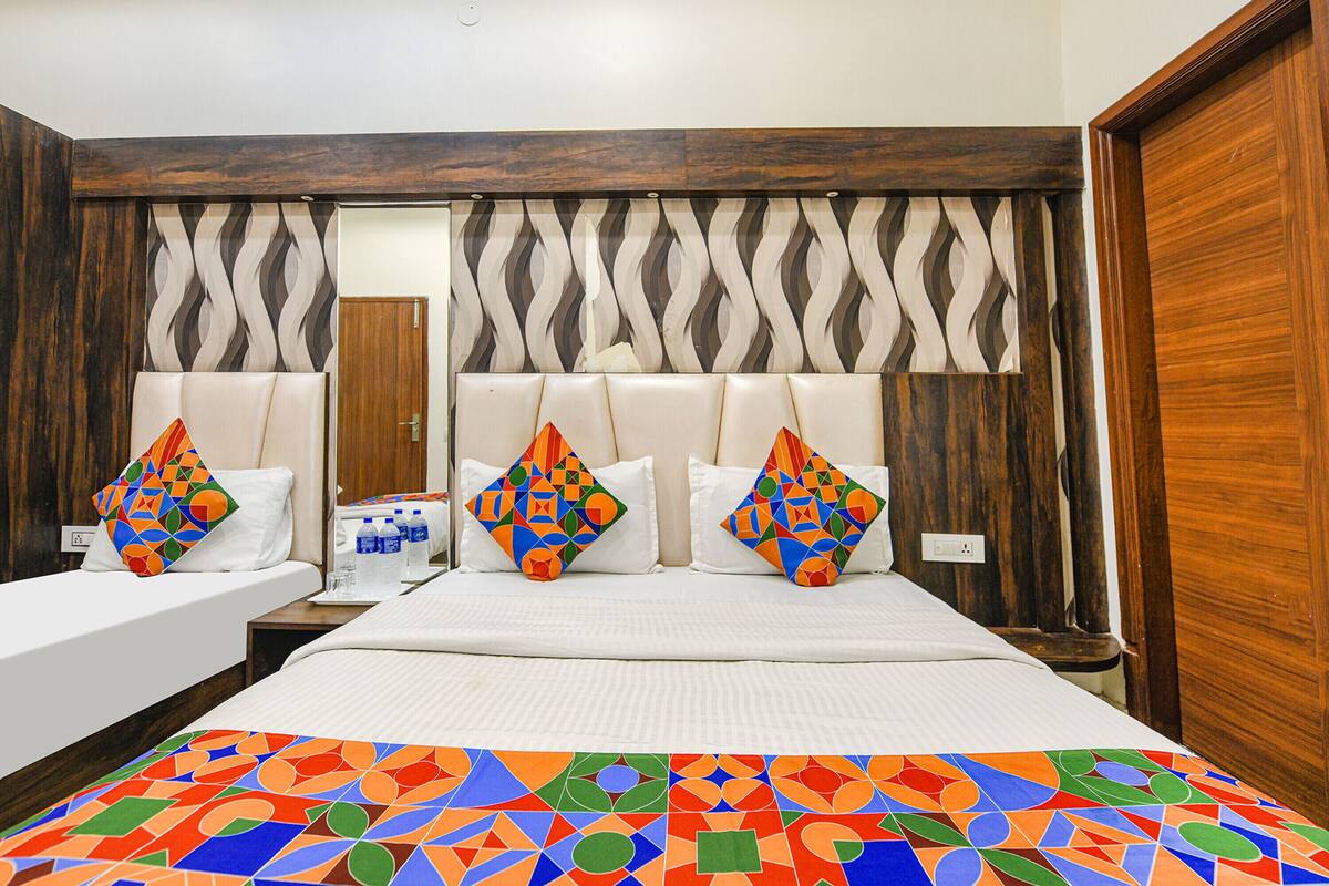 A hotel room with two beds, a large bed with a colorful geometric-patterned bedspread, and a smaller bed with a plain white bedspread.