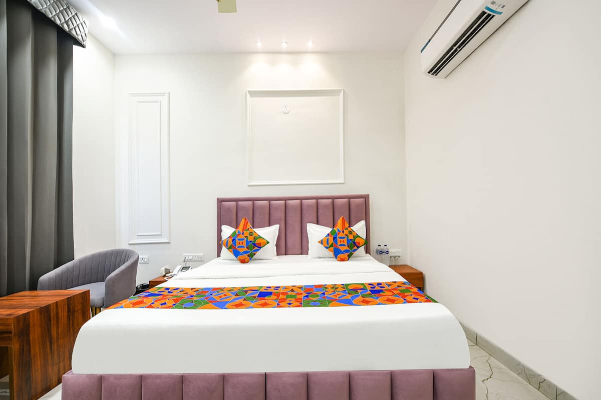A hotel room with a bed, a chair, a bedside table, and an air conditioning unit.