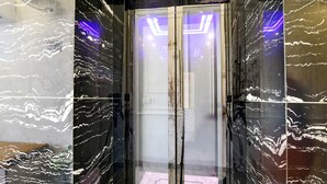 Een moderne lift met glanzende marmeren wanden en een glazen deur.