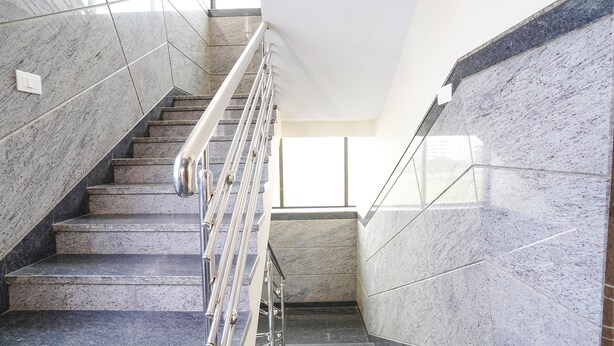 Un escalier en marbre avec des rampes métalliques menant à un palier.