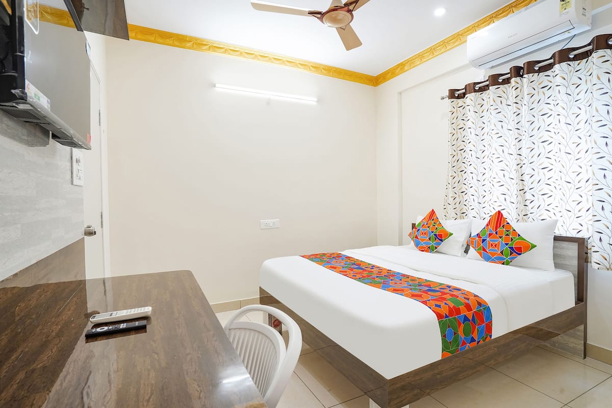 A hotel room with a bed, a desk, a chair, a ceiling fan, and an air conditioning unit.