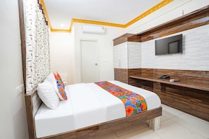 A modern hotel room with a bed, a TV mounted on the wall, and a wooden desk.