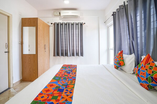 A hotel room with a bed, a wardrobe, a window with curtains, and an air conditioning unit.
