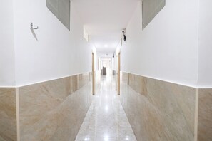 A long, narrow hallway with white walls and marble flooring.