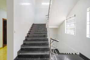 Uma escadaria com degraus pretos e corrimãos de metal, que leva a um patamar com janela.