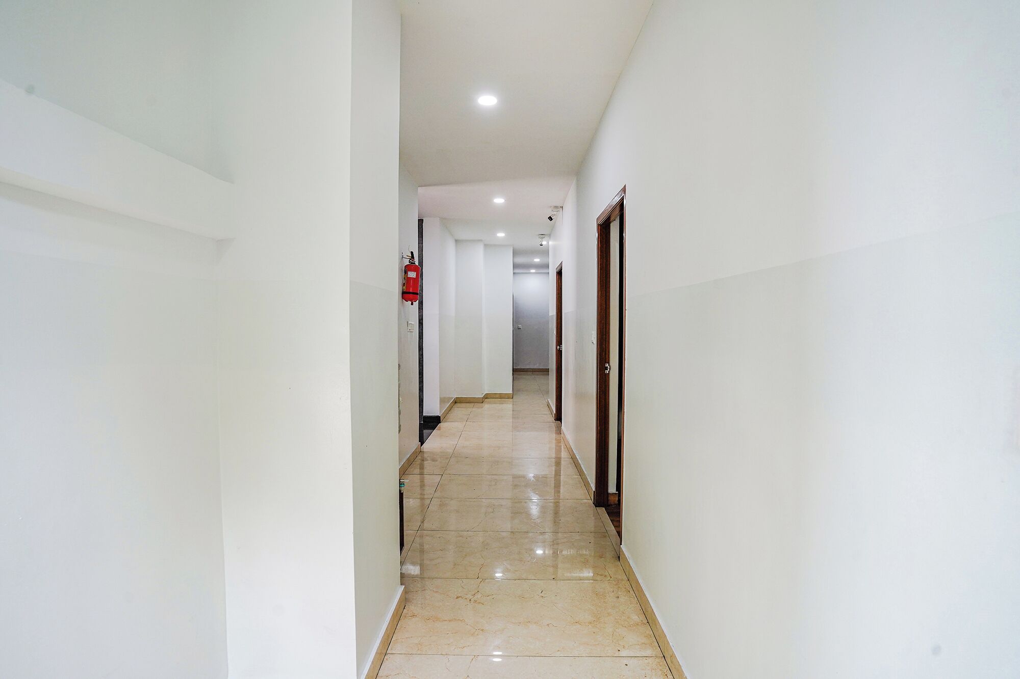 A corridor with white walls, a fire extinguisher, and a door at the end.
