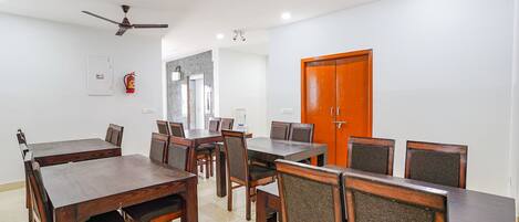 Un comedor con varias mesas y sillas de madera, un ventilador de techo y un extintor en la pared.