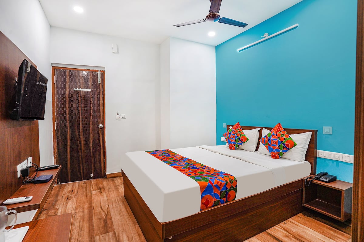 Quarto de hotel com cama de madeira, ventilador de teto, televisão, mesa de cabeceira e criado-mudo.