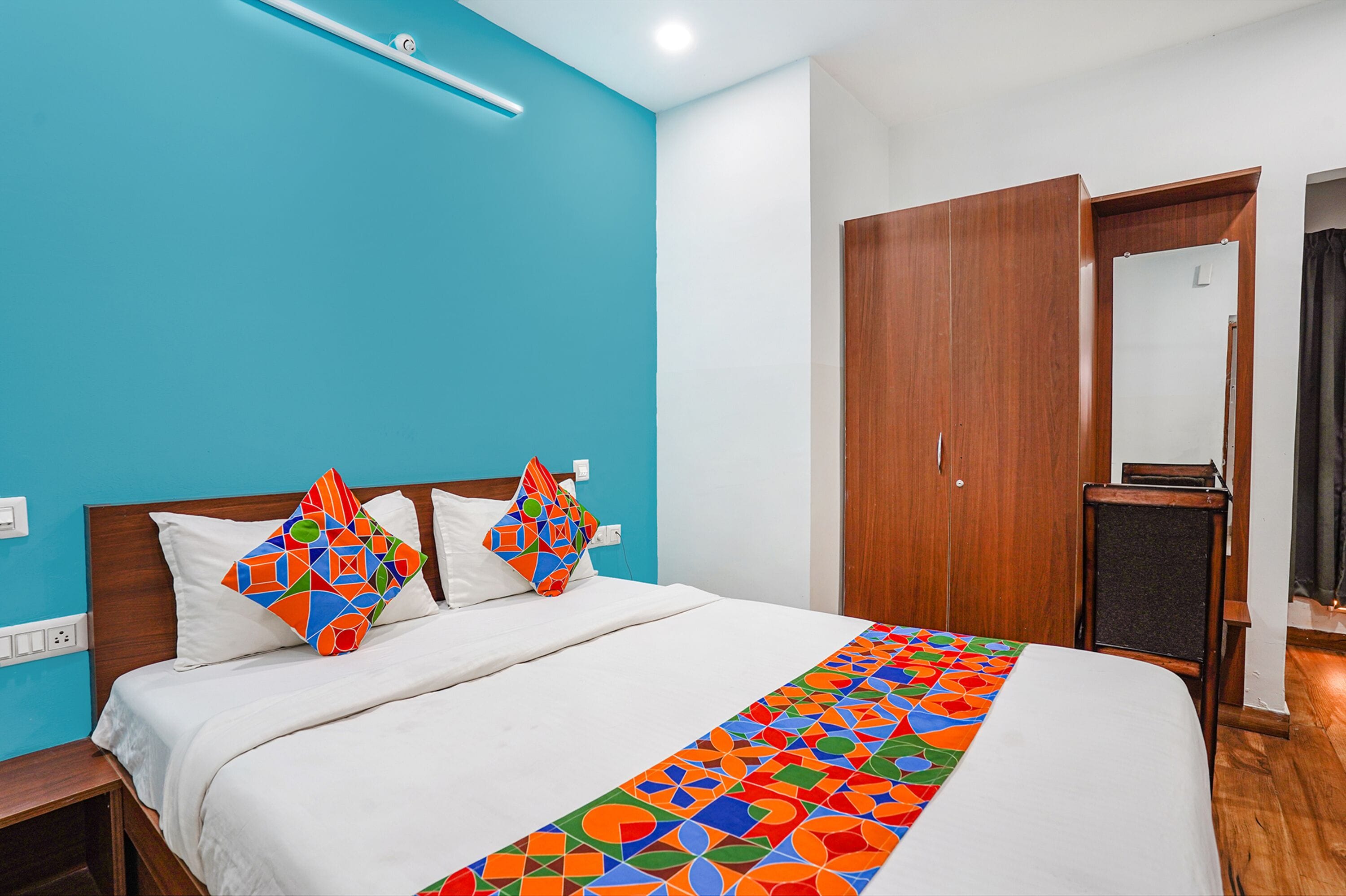 A hotel room with a bed, a wooden wardrobe, and a mirror.
