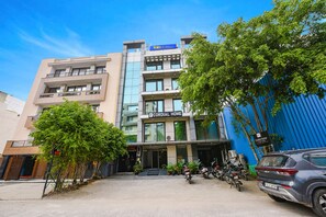 A multi-story building with a sign for 'Cordial Home' and 'Fab Hotels'. There are several motorcycles parked in front, and a blue structure to the right. - Fabhotel Cordial Home (New Delhi)